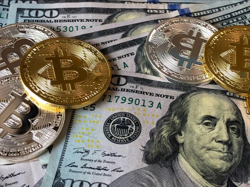U.S. dollar bills and gold Bitcoin coins arranged together
