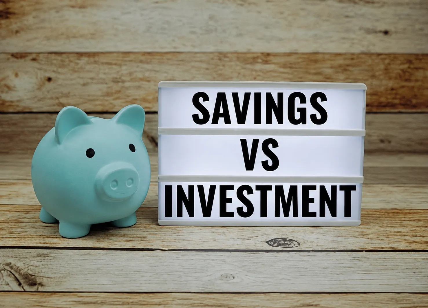 Piggy bank next to illuminated Savings vs Investment letters