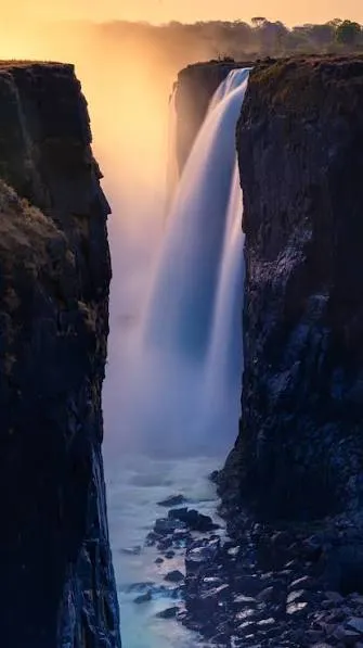 Victoria Falls dropping between dark gorge cliffs in golden light