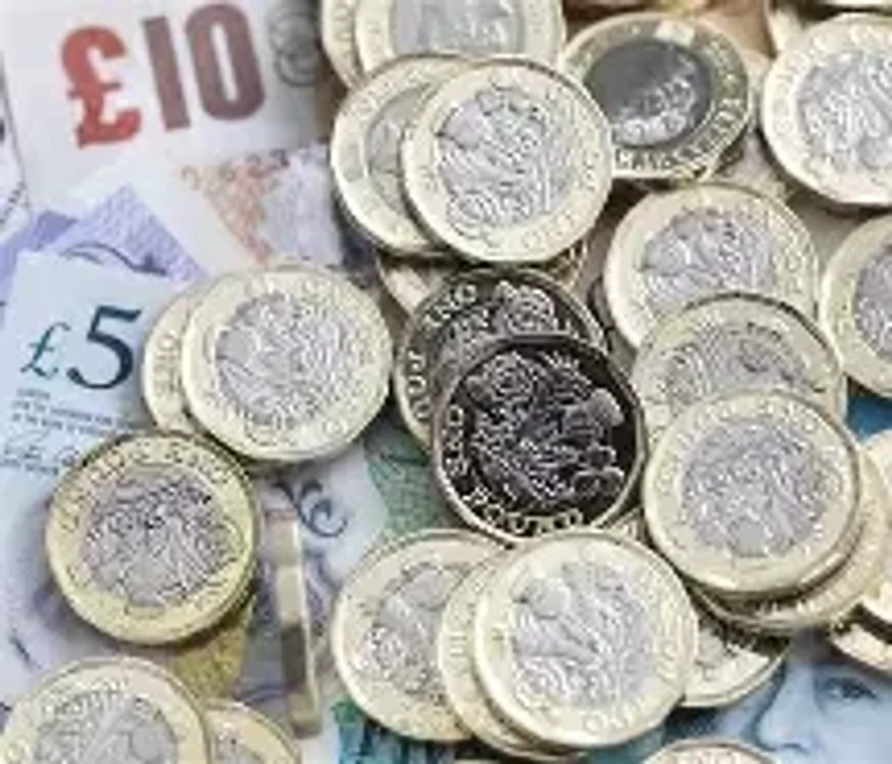 A pile of British pound coins and notes showing the £10 and £5 notes with silver and brass coins