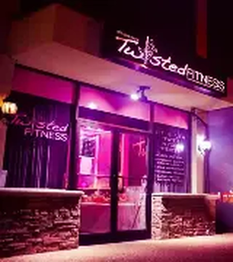 Twisted Fitness studio storefront at night with pink neon window lettering, dark brick, and glass frontage