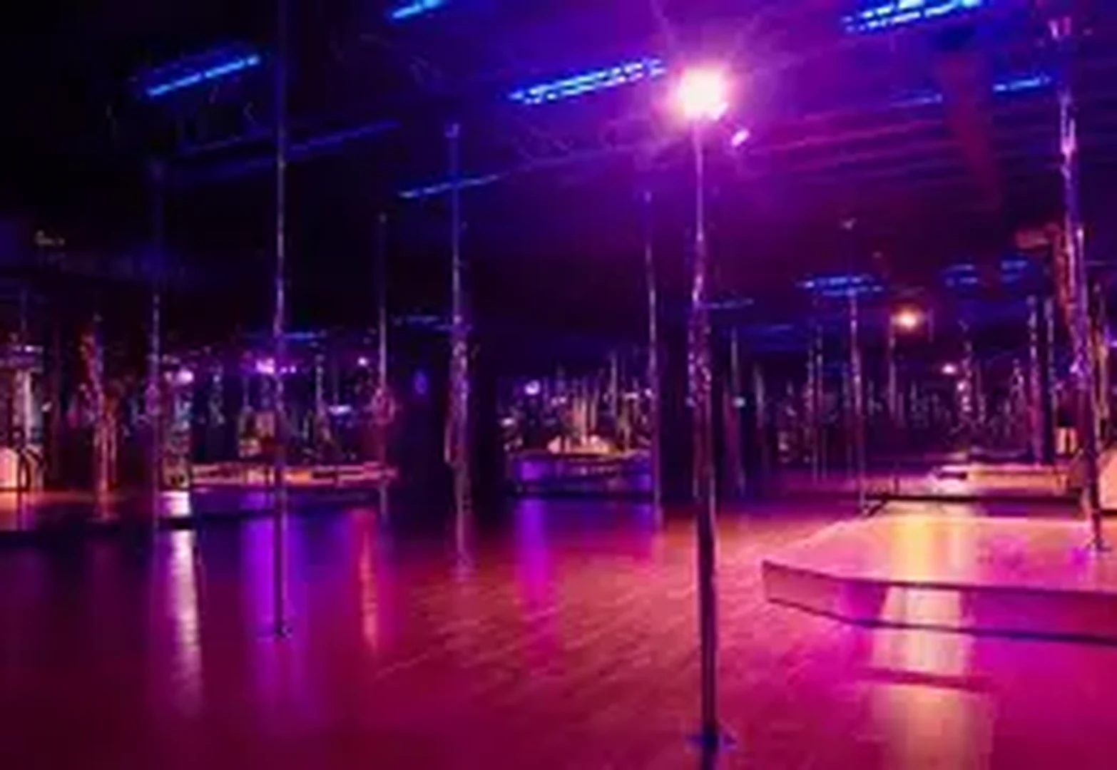 Twisted Fitness studio interior with rows of poles on a polished wooden floor under pink and purple uplighting