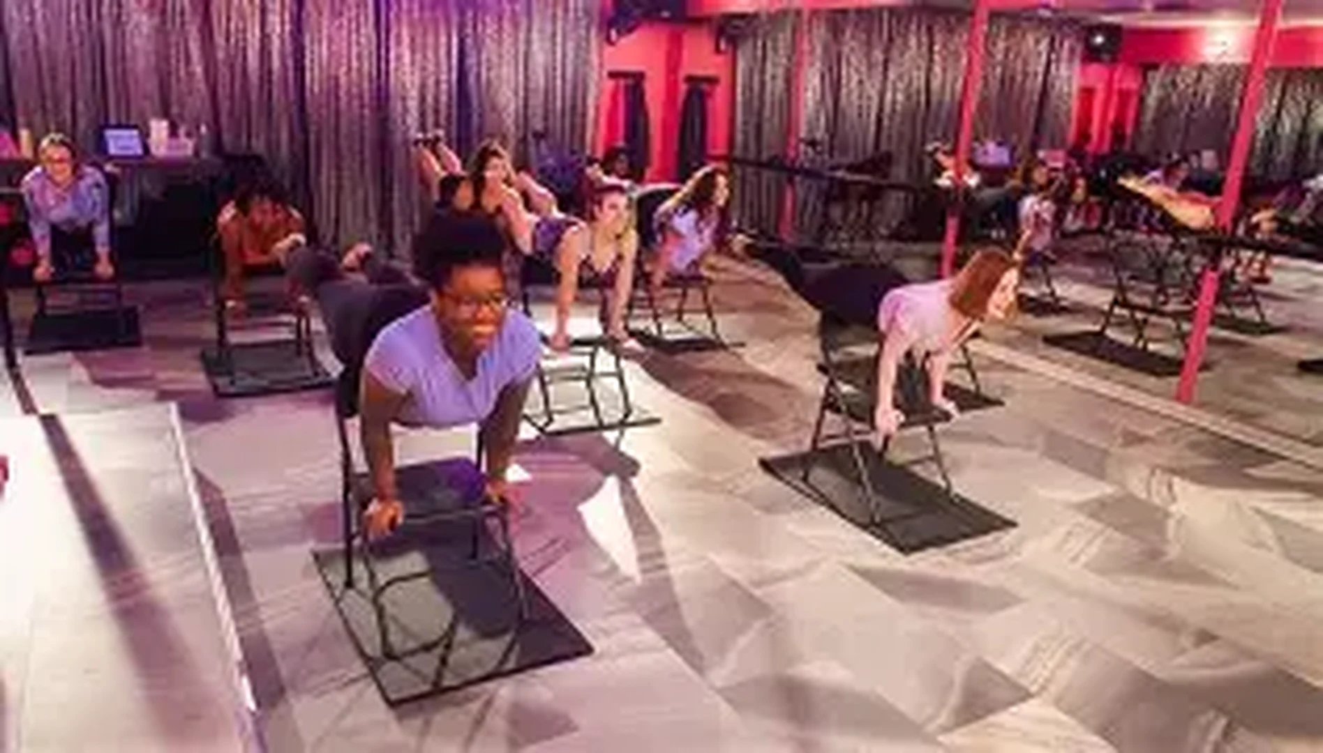 Chair-dancing class with women working on black chairs in a mirrored pink studio