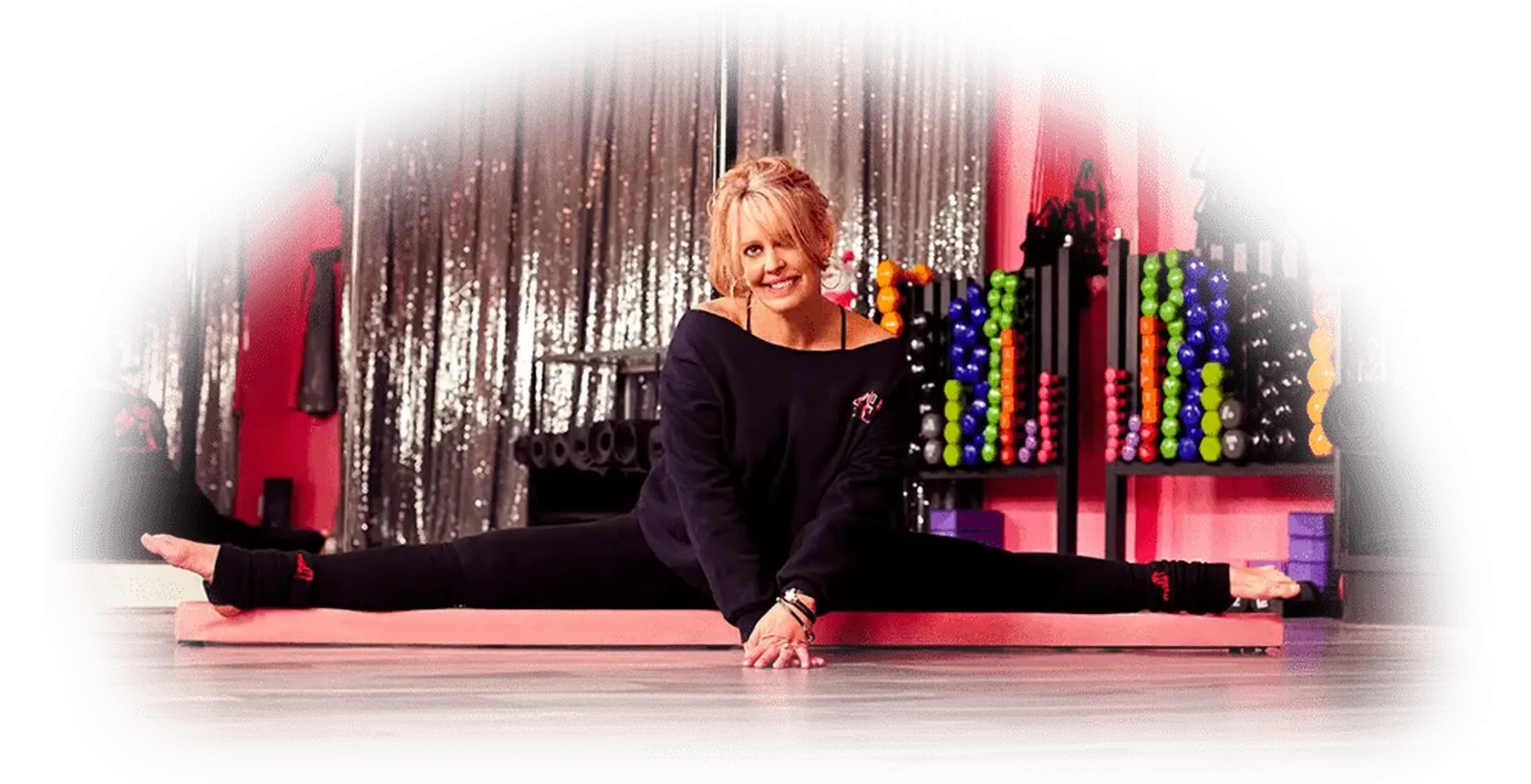 Twisted Fitness owner Rio smiling while seated in a full side split on a pink mat in the mirrored studio