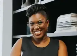 Natacha Pennycooke laughing in a black sleeveless top in front of dark bookshelves