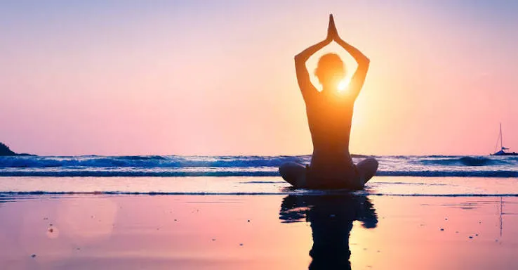 A person meditating on the beach at sunset